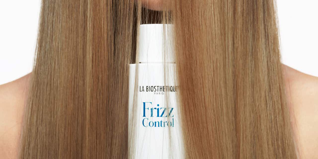 Flacon shampooing Frizz Control de La Biosthétique devant une chevelure longue